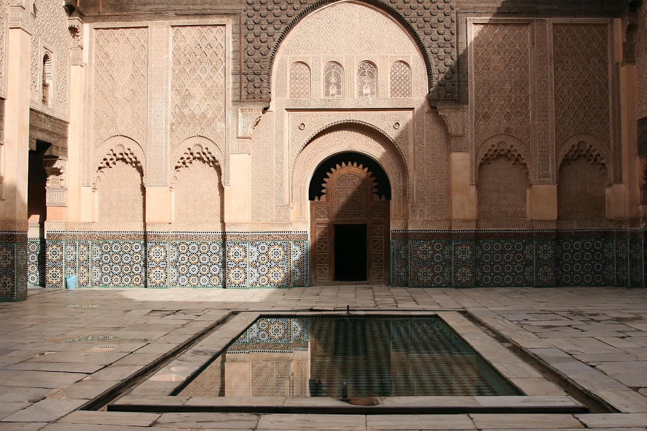 A long shallow reflecting basin in a tiled courtyard, arcade doubled in the water