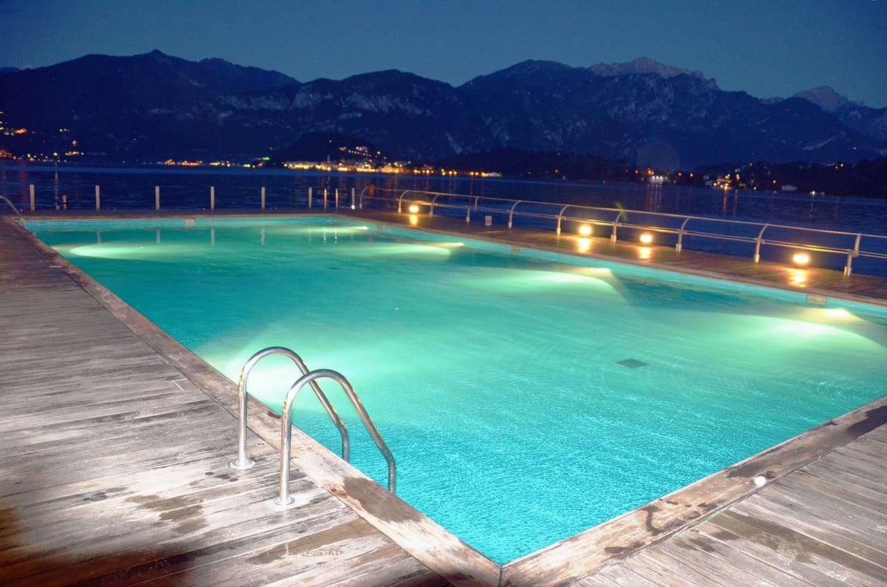 An infinity pool at dusk overlooking a lake and hills, lit from within
