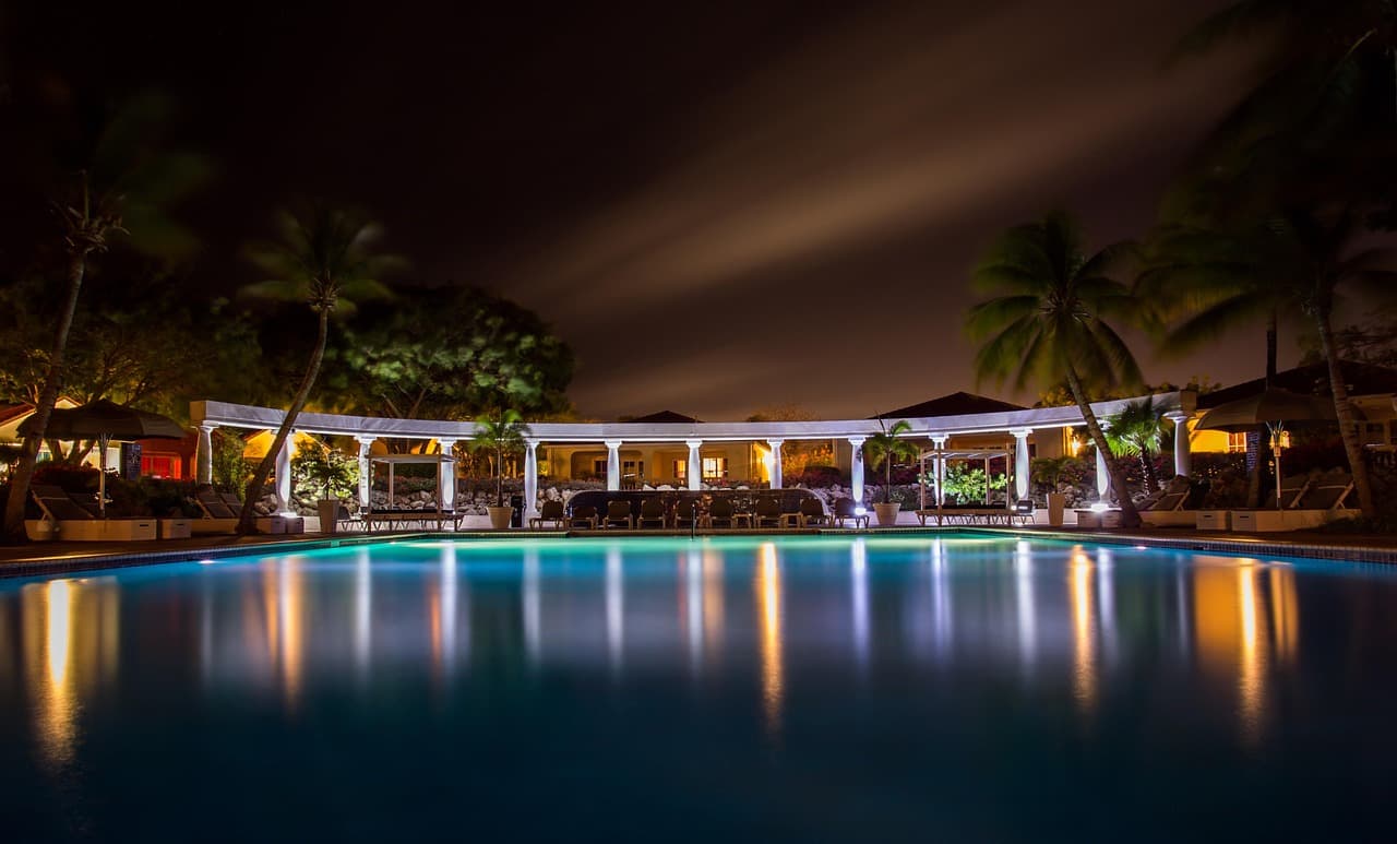 A lit rectangular pool at night with palms reflected in the still surface