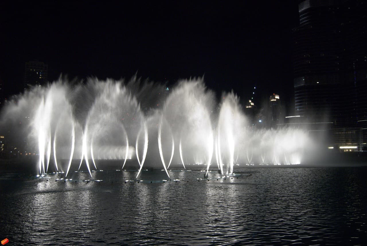 Rows of illuminated fountain jets rising from dark water at night